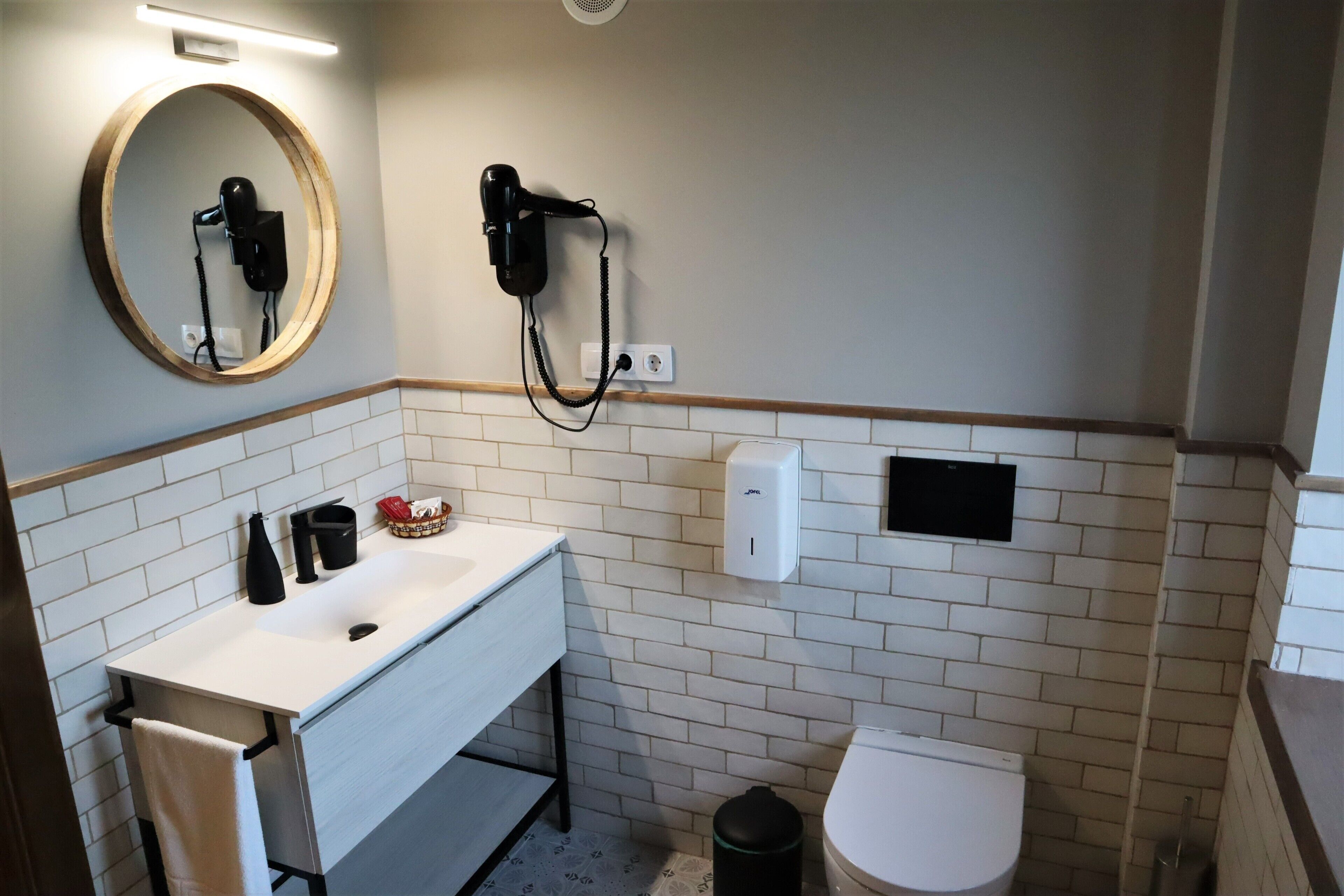 Un baño con lavamanos blanco, espejo, secador de pelo y retrete.