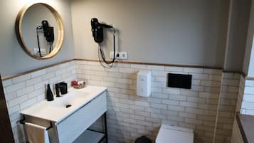Un baño con lavamanos blanco, espejo, secador de pelo y retrete.