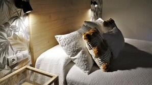 A bedroom with a wooden headboard, a white textured bedspread, and a decorative pillow with a brown accent. - Eguen Goiko (Ispaster)