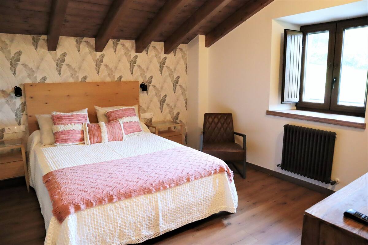 A bedroom with a wooden bed, a chair, a window with blinds, and a radiator.