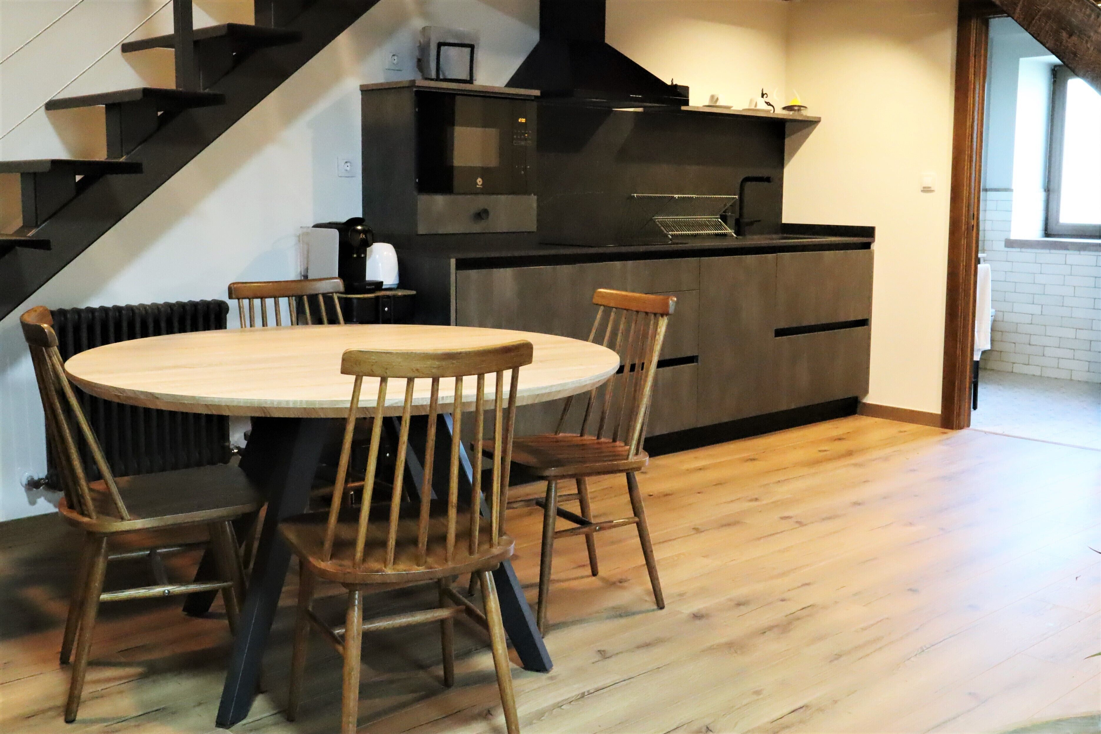 Een moderne keuken met een centraal eiland, houten stoelen en een trap.