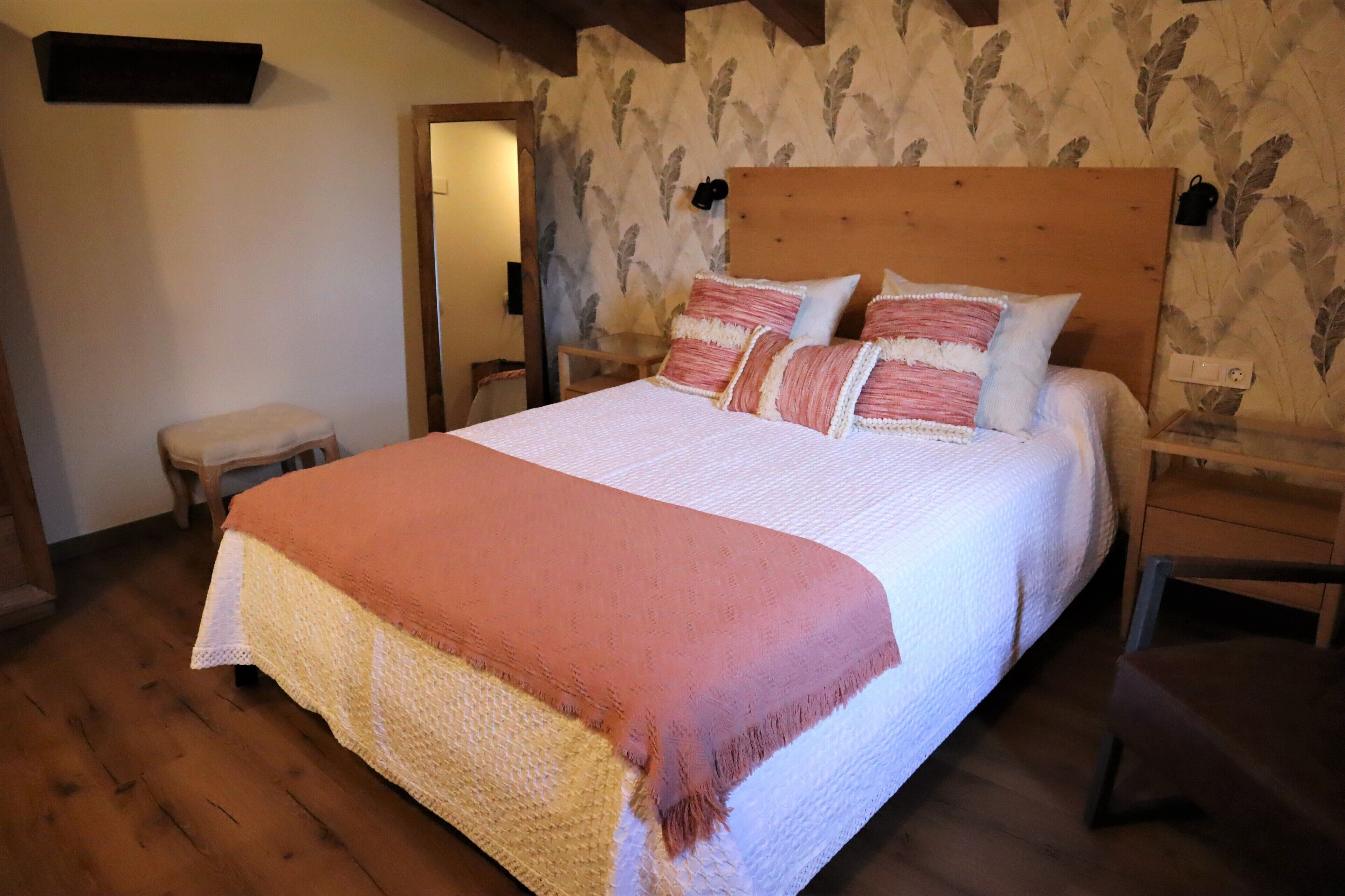 A neatly made bed with a patterned bedspread and pillows, a wooden headboard, and a small bedside table with a lamp.