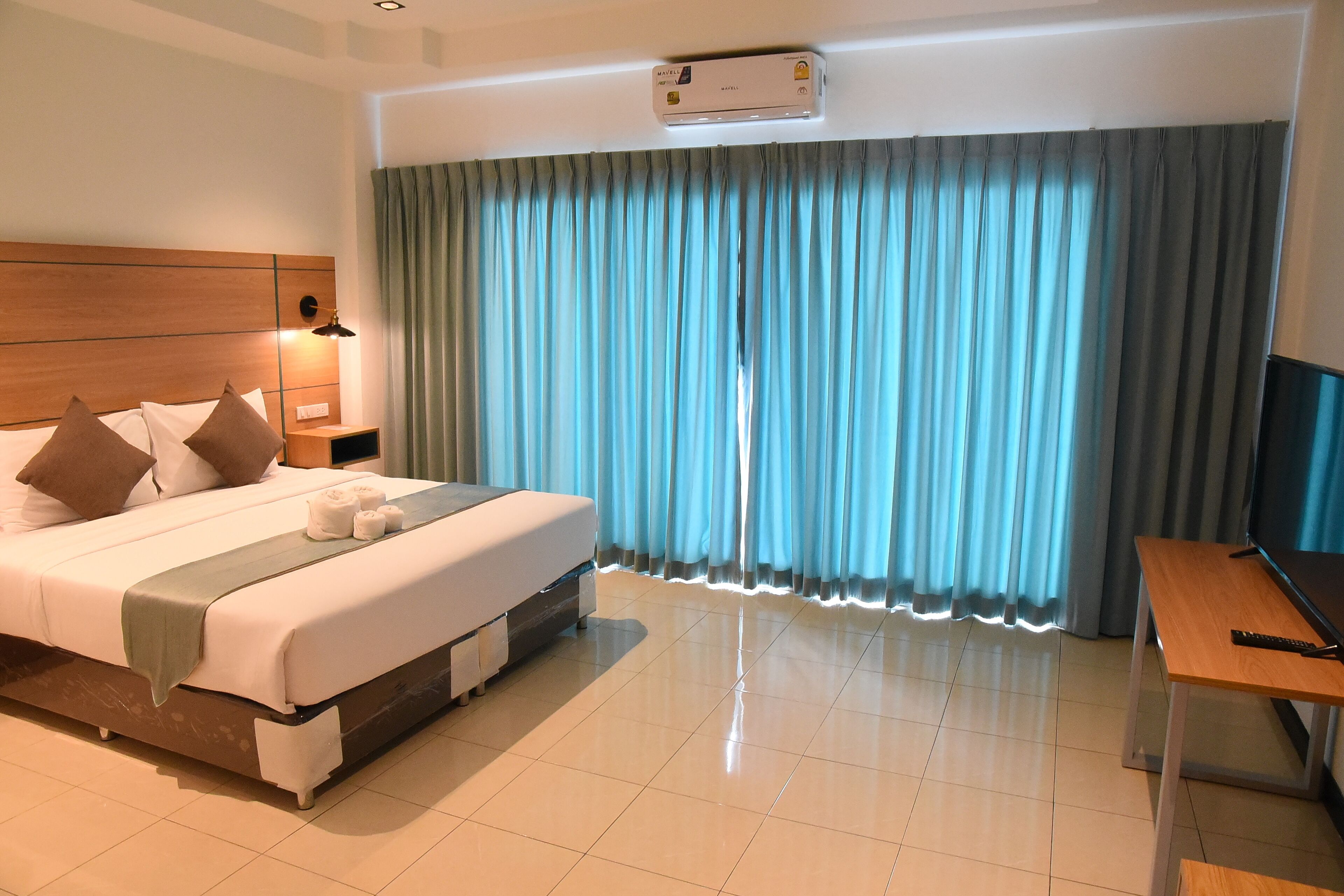 Habitación de hotel con cama, escritorio, televisor y ventana con cortinas.