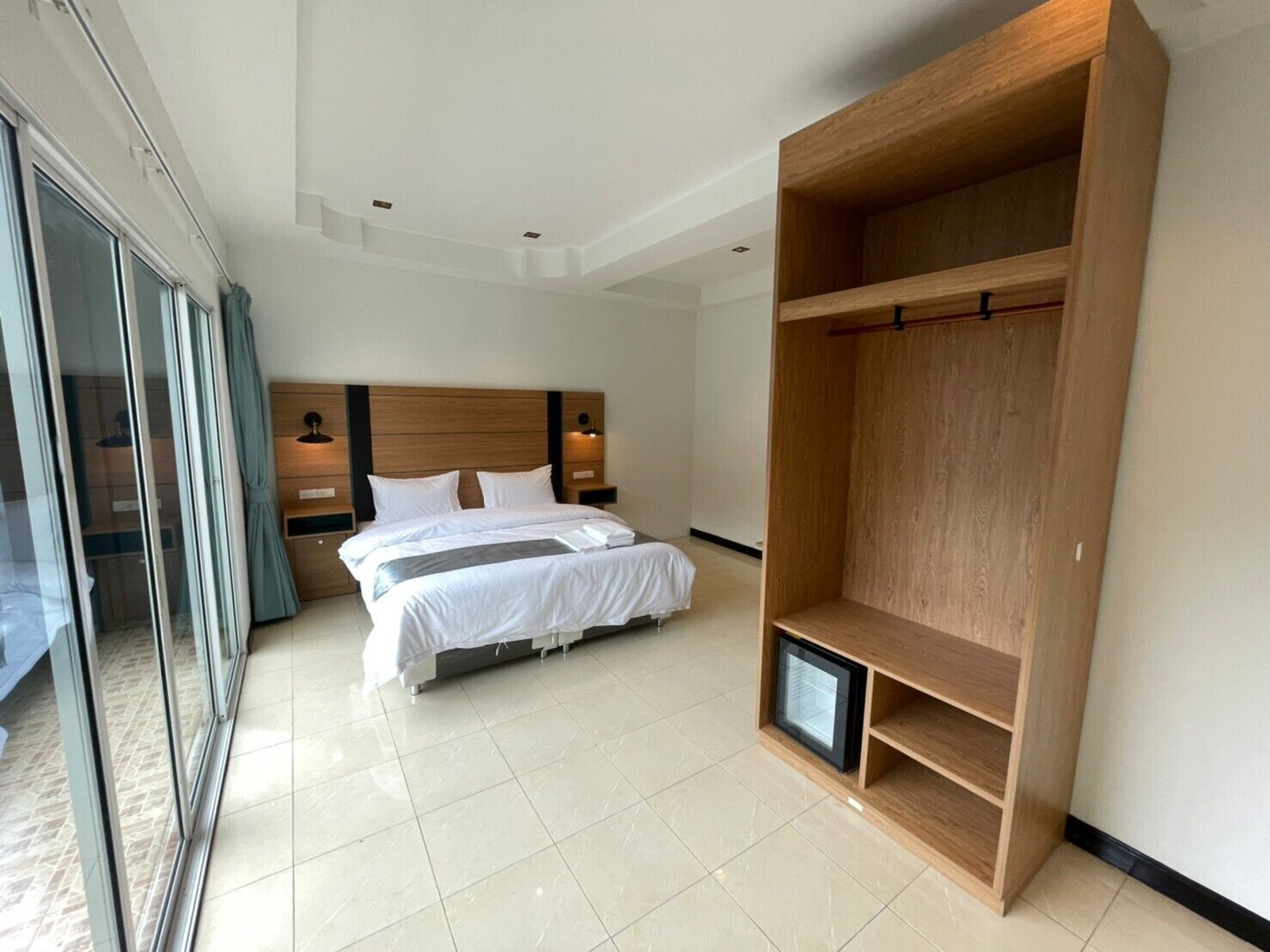 Une chambre d’hôtel moderne avec un grand lit, une armoire en bois et une porte-fenêtre coulissante donnant sur un balcon.