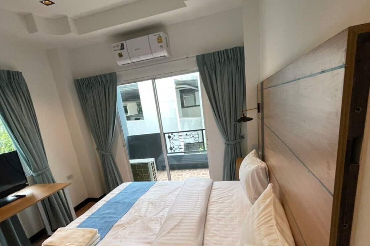 A hotel room with a bed, a TV, a desk, and a balcony with curtains.