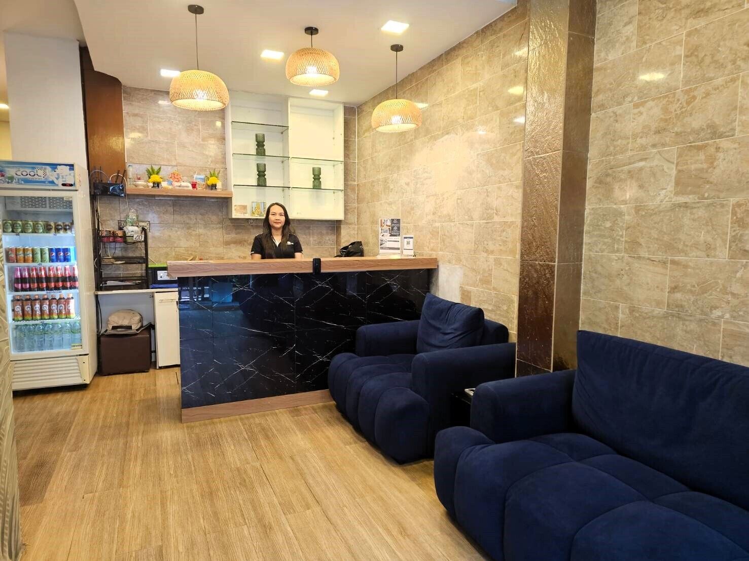 A reception area with a marble counter, a refrigerator stocked with beverages, and a seating area with blue sofas.