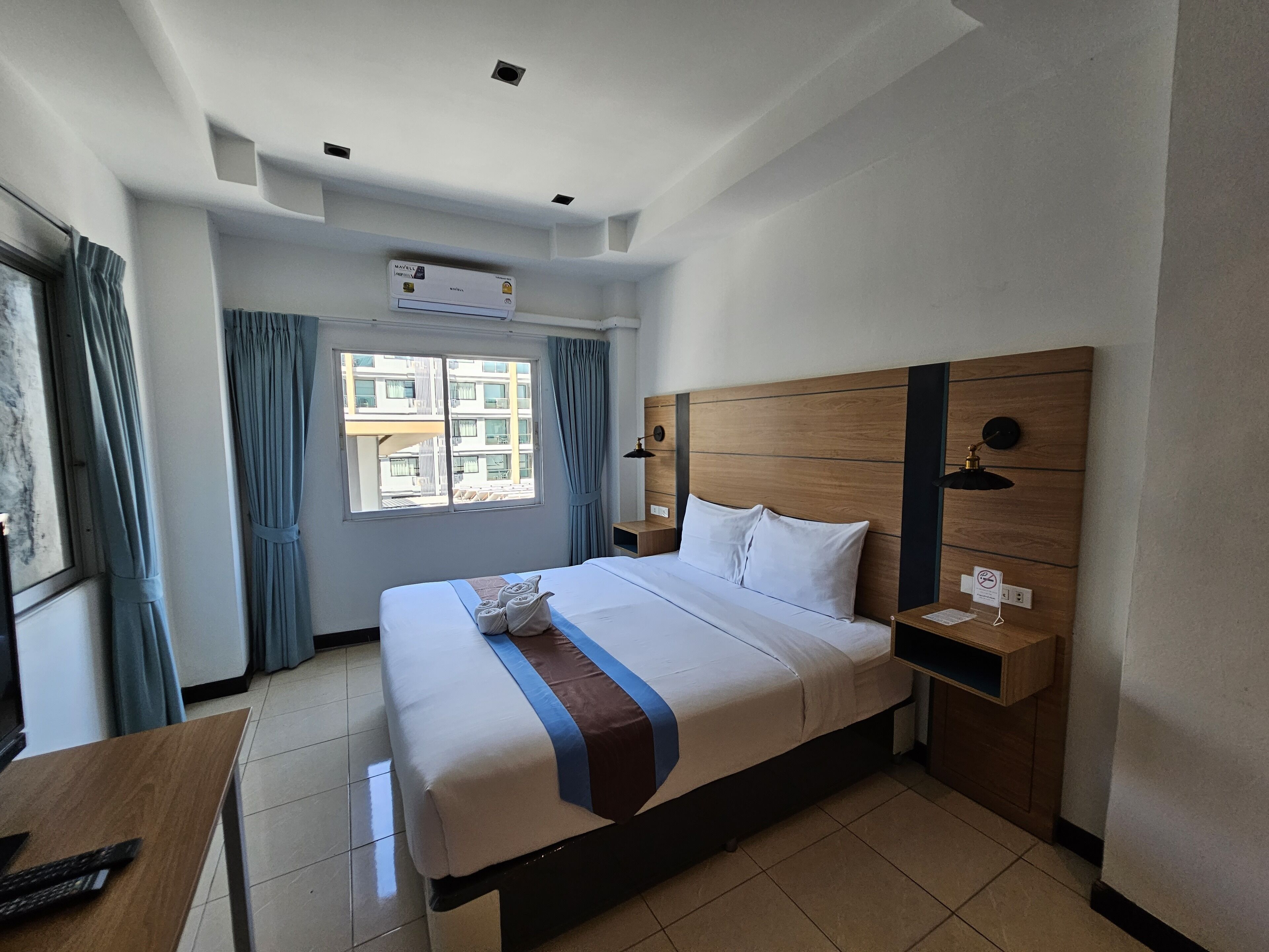A hotel room with a large bed, a wooden headboard, a desk with a keyboard, and a window with curtains.
