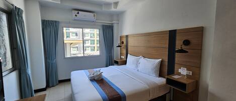 Ein Hotelzimmer mit einem großen Bett, einem hölzernen Kopfteil, einem Schreibtisch mit Tastatur und einem Fenster mit Vorhängen.