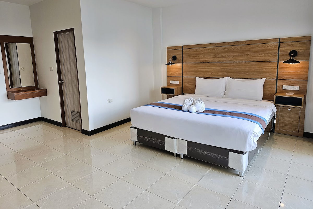 A hotel room with a large bed, wooden headboard, two bedside tables with lamps, a mirror, and a door.