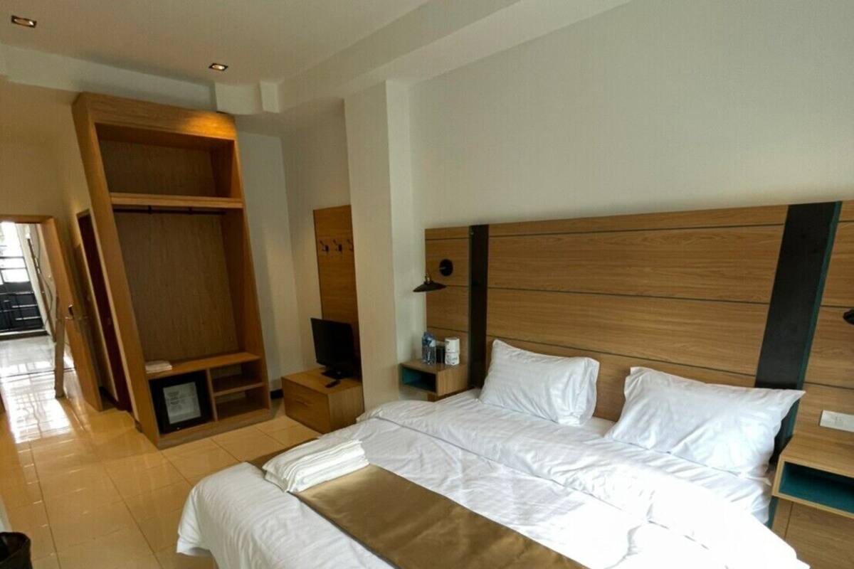 A hotel room with a large bed, wooden headboard, bedside tables, and a wardrobe.