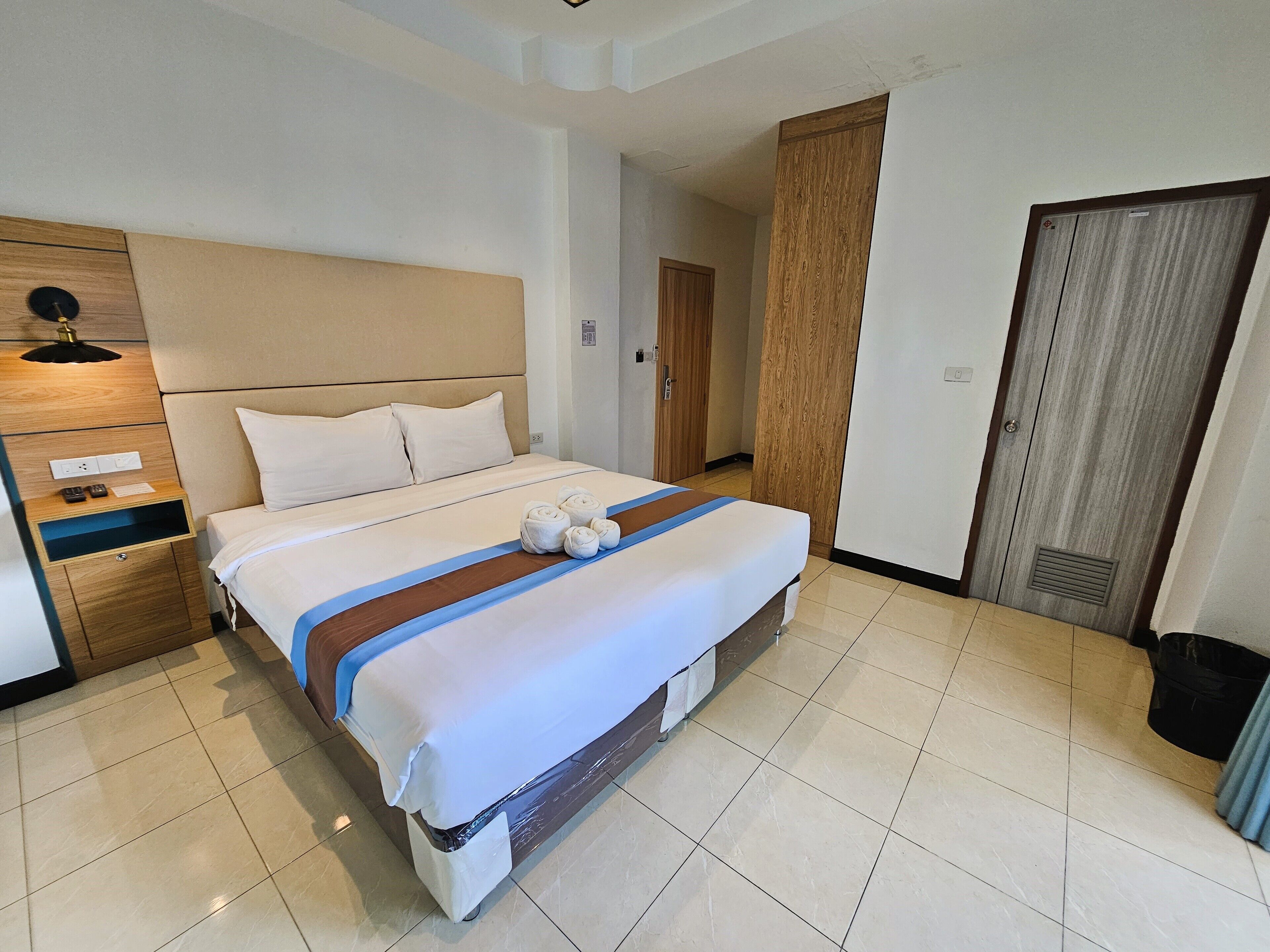 A hotel room with a bed, a wooden nightstand, a wardrobe, and a bathroom door.