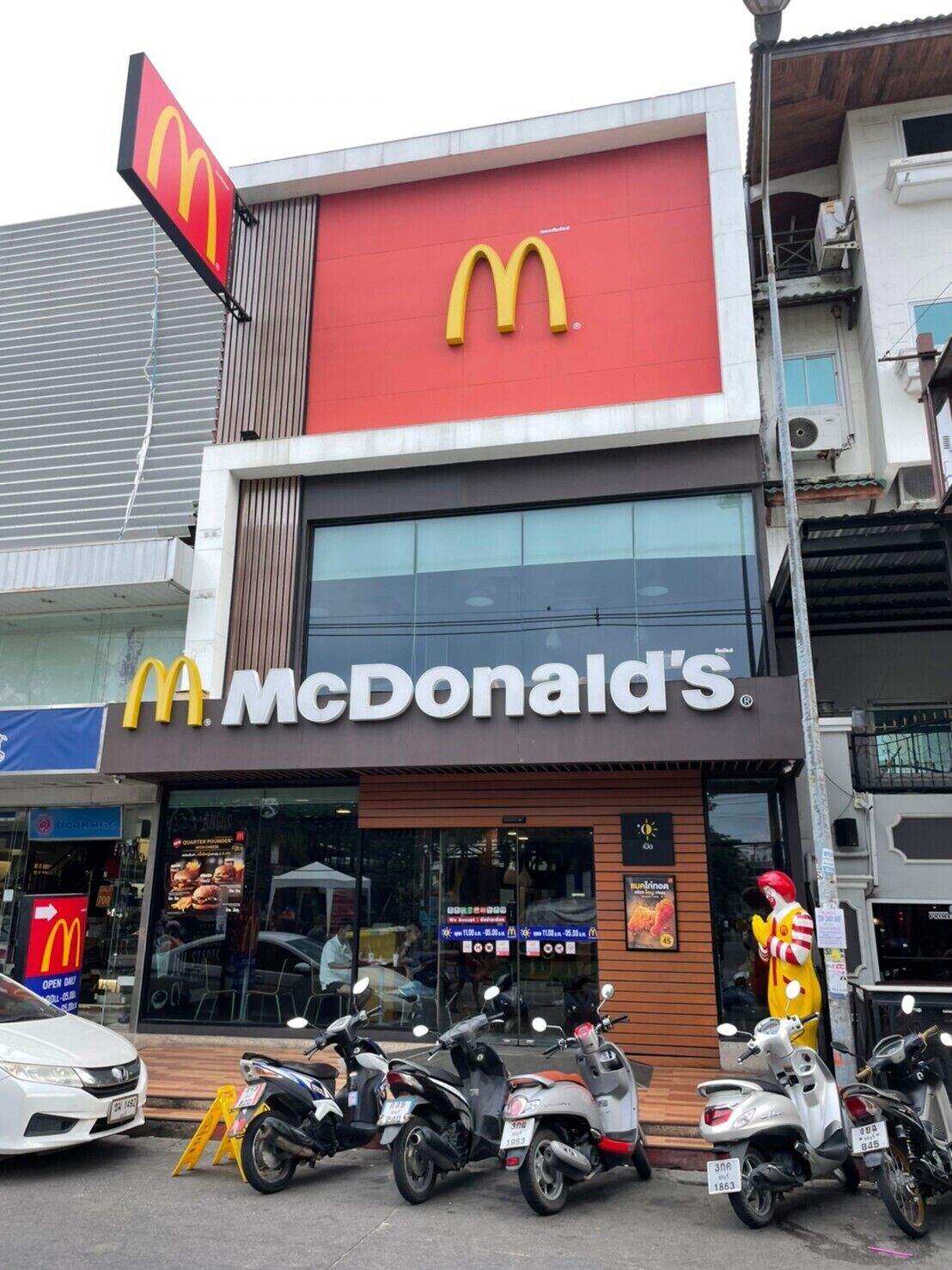 A McDonald's restaurant with a large sign, a glass storefront, and several parked scooters in front.