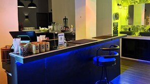 Eine Bar mit blau beleuchteter Theke, schwarzen Pendelleuchten und einer Sitzgruppe mit blauen Hocker.
