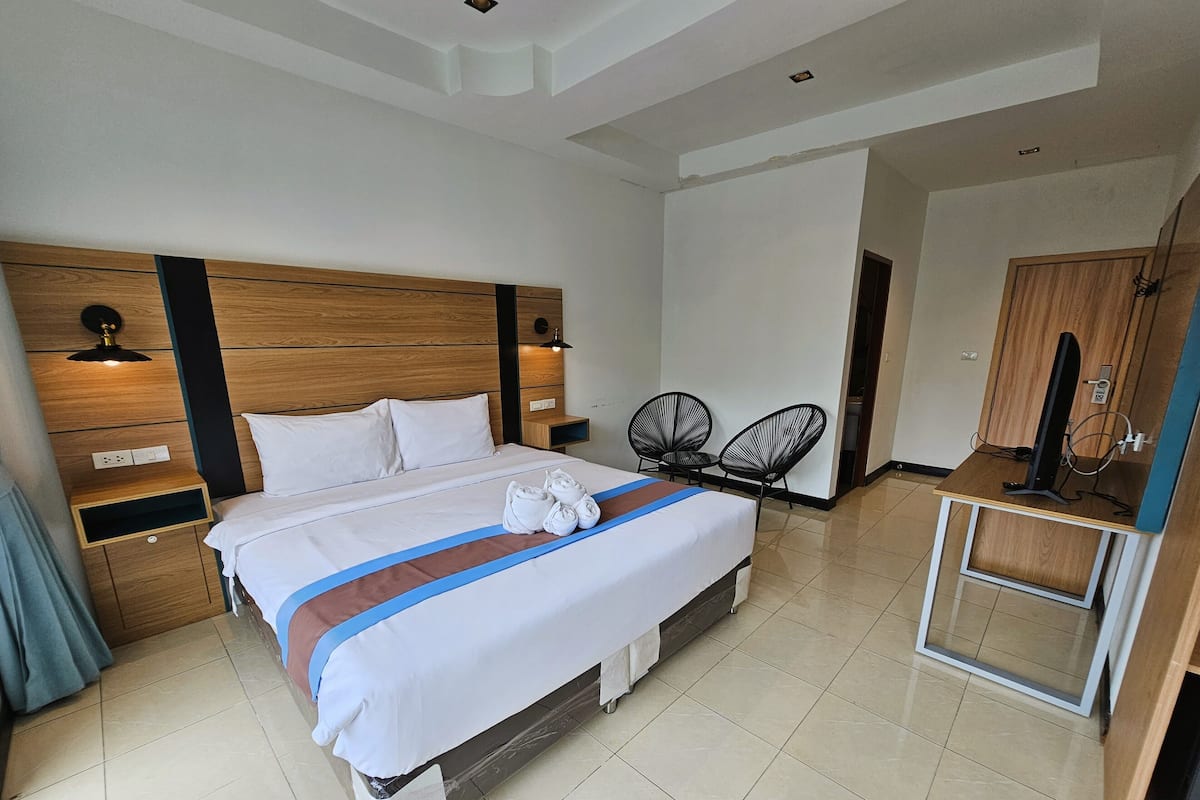 A hotel room with a large bed, wooden headboard, two bedside tables, a desk with a computer, and two chairs.