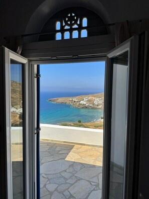 A view through a glass door to a coastal area with a clear sky, a road, and buildings.