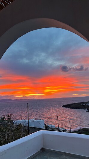 A sunset view through an archway overlooking the sea and a coastal landscape.