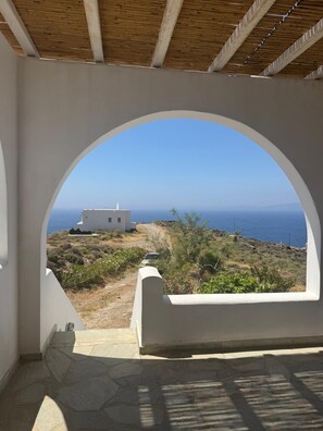 A room with a view of the sea, a white building, and a stone pathway.