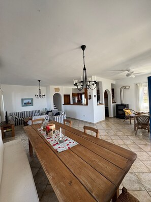 A spacious living area with a wooden dining table, a chandelier, and a ceiling fan.