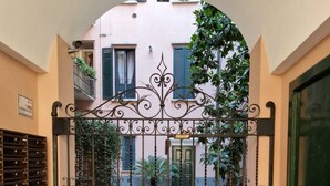 A gated courtyard with a tiled floor, potted plants, and a building with a balcony. - Cozy flat mins walk to Navigli and metro Porta Genova [NEW] (Milano)