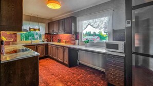 Une cuisine moderne avec des meubles en bois foncé, un réfrigérateur en acier inoxydable et une fenêtre donnant sur une maison et des arbres.