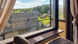 Une pièce dotée d’une grande fenêtre donnant sur un paysage rural, d’un bureau en bois et d’une chaise.