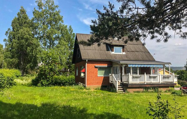 Ett tvåvåningshus med en fasad av rött tegel, ett sadeltak och en täckt veranda med vita räcken.