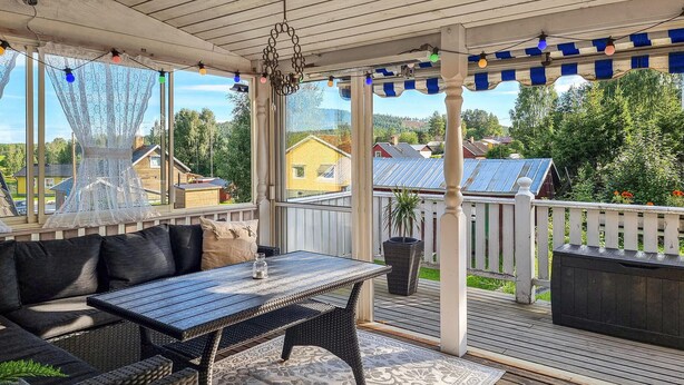 Un espace extérieur abrité, aménagé avec une table et des chaises, un rideau décoratif en dentelle et offrant une vue sur le quartier.