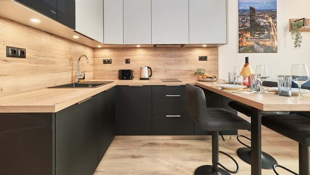 Una cocina moderna con armarios negros, encimera de madera y una zona de comedor con una mesa para dos.