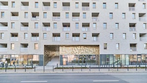 Un edificio de varios pisos con balcones, un acceso con diseños y fachada de vidrio.