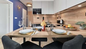 Un comedor moderno con una mesa de madera preparada para dos personas, una cocina al fondo y una pared azul de acento.