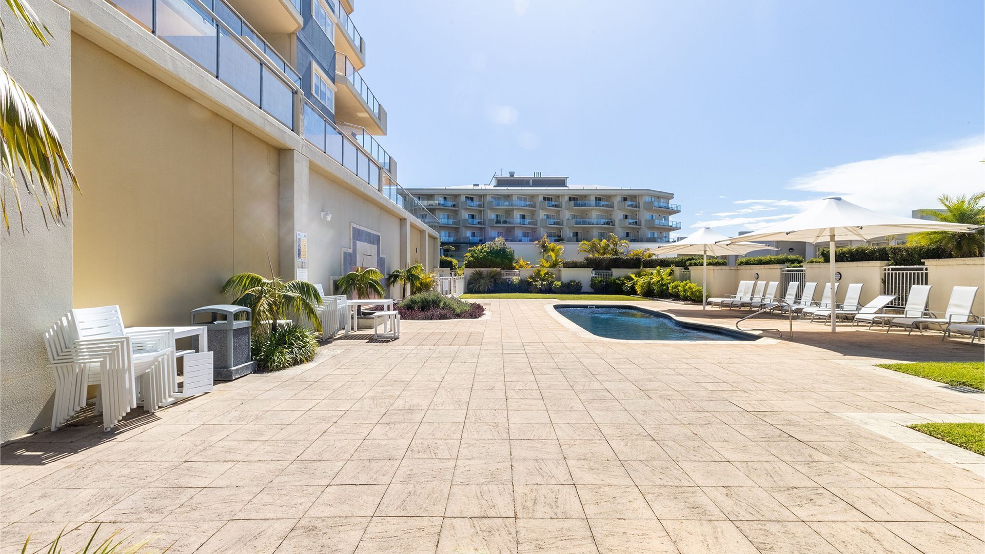A hotel courtyard with a swimming pool, lounge chairs, and a building with multiple balconies.