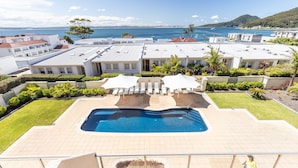 A pool area with a view of the ocean, surrounded by buildings and greenery. - 203 The Breakwater, 2 Messines St - magical unit with lift, pool, views and aircon (Shoal Bay)