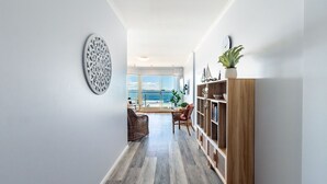 A modern living room with a view of the sea, a wooden bookshelf, and a round decorative wall piece. - 203 The Breakwater, 2 Messines St - magical unit with lift, pool, views and aircon (Shoal Bay)