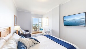 A hotel room with a large bed, a TV on the wall, a balcony with a view of the sea, and a chair by the window. - 203 The Breakwater, 2 Messines St - magical unit with lift, pool, views and aircon (Shoal Bay)