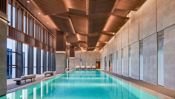 Una piscina interior con diseño moderno, amplios ventanales y techo de listones de madera.