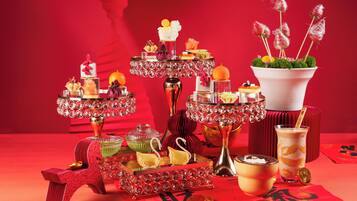 Une table dressée avec divers plats et boissons, notamment un verre de café glacé et un bol de soupe, sur une nappe rouge ornée de caractères chinois.