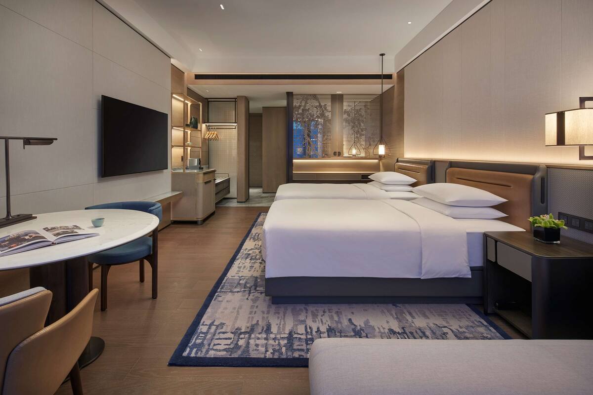 Una habitación de hotel moderna con una cama grande, un escritorio, una silla, un televisor y una mesita de noche con una lámpara.