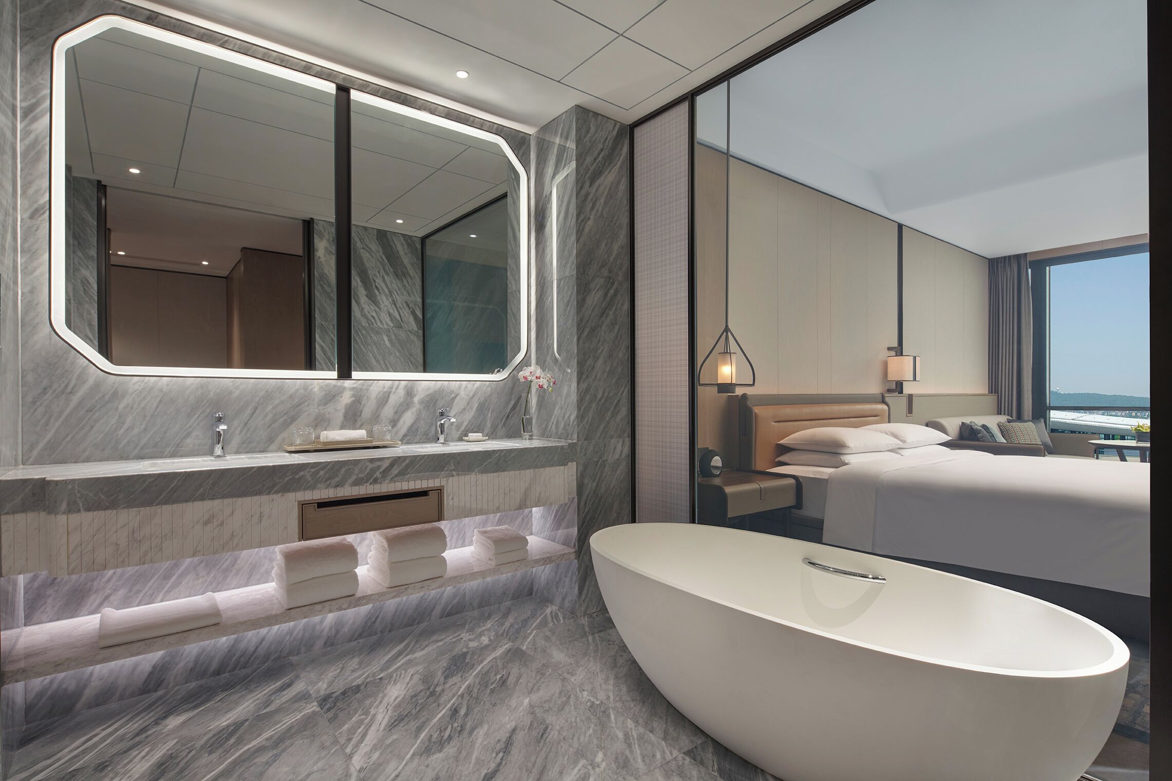 Un bagno d'hotel moderno con una vasca da bagno indipendente di grandi dimensioni, un mobile vanitario in marmo e uno specchio ampio.