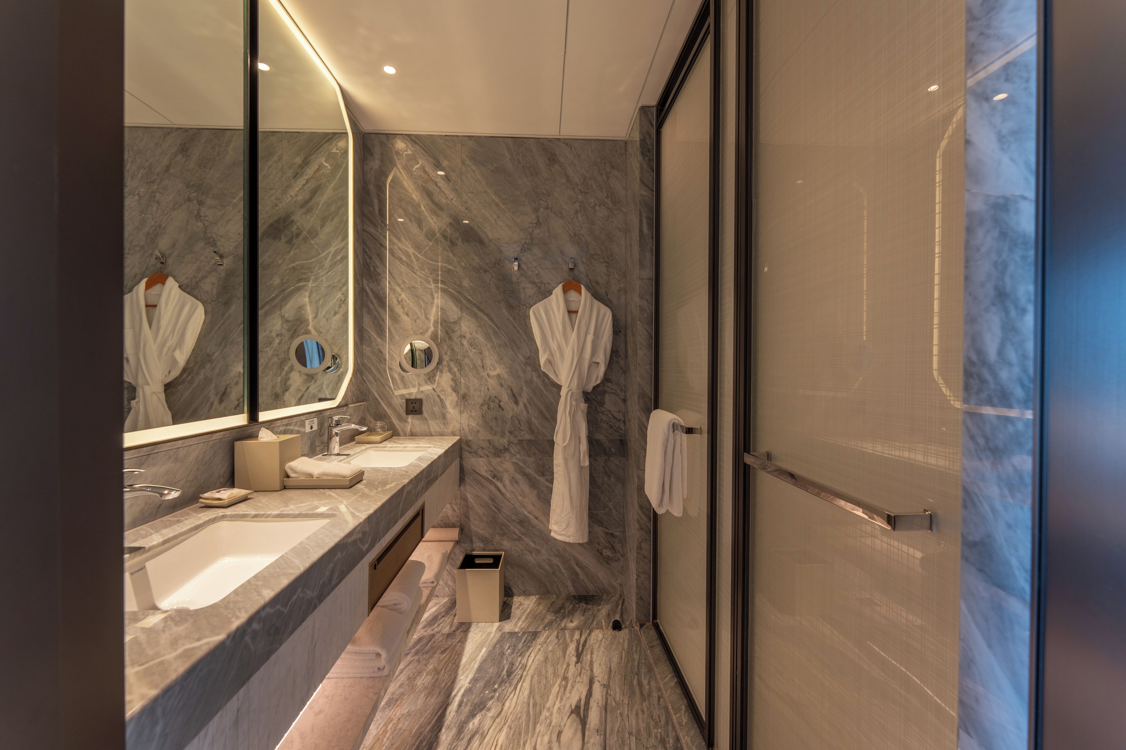 A modern bathroom with a marble sink, a large mirror, and a glass shower enclosure.