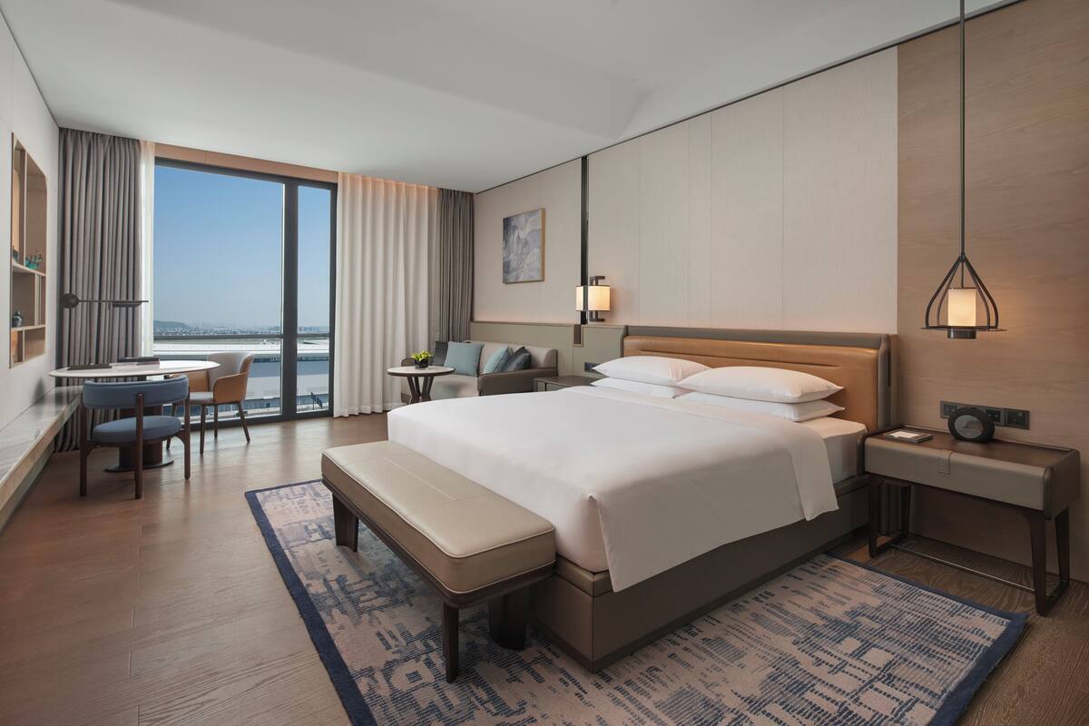 Una habitación de hotel moderna con una cama grande, un escritorio, una silla y vistas a la ciudad.