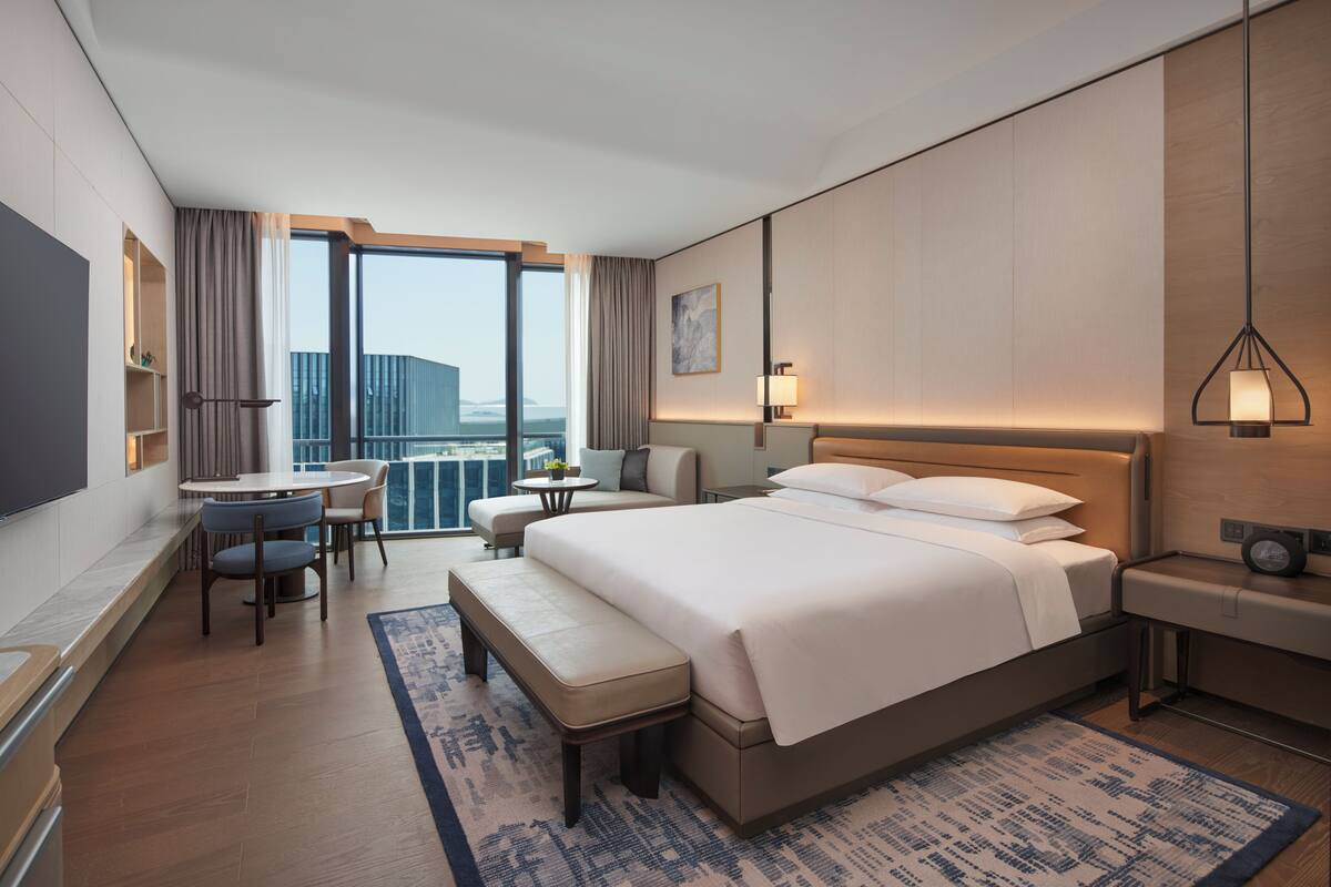 Una habitación de hotel moderna con una cama grande, un escritorio, un sofá y vistas a la ciudad.