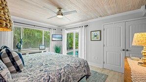 A bedroom with a bed, a ceiling fan, a television, and a view of the outdoors. - Peaceful Holmes by Beach Boutique Rentals (Holmes Beach)