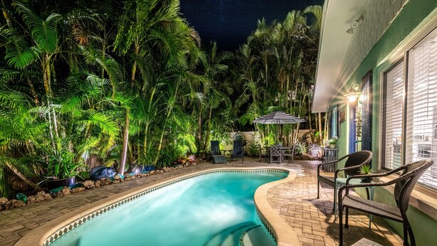 A swimming pool surrounded by lush greenery, with a patio area featuring chairs and a table. - Peaceful Holmes by Beach Boutique Rentals (Holmes Beach)
