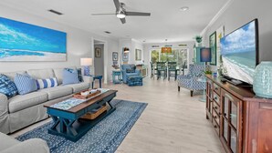 A spacious living room with a large sofa, a coffee table, and a dining area with chairs and a table. - Peaceful Holmes by Beach Boutique Rentals (Holmes Beach)