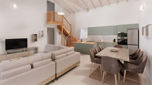 A modern living room with a sofa, TV, and dining area with chairs. - Nisos Green Villa, Private Beach & Pool (Corfu)