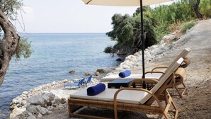 A beachside lounge area with wicker chairs and a large umbrella, overlooking the sea. - Nisos Green Villa, Private Beach & Pool (Corfu)