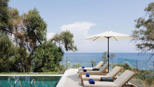A poolside area with lounge chairs and an umbrella, overlooking a body of water. - Nisos Green Villa, Private Beach & Pool (Corfu)