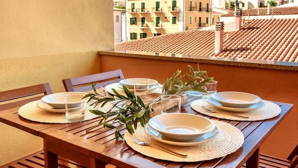 A wooden table set with plates, glasses, and cutlery on a balcony with a view of buildings. - Residence con piscina a 300 mt dal mare (Santa Teresa di Gallura)