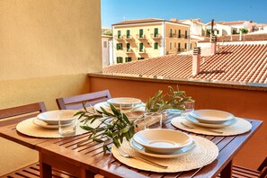 A wooden table set with plates, glasses, and cutlery on a balcony with a view of buildings. - Residence con piscina a 300 mt dal mare (Santa Teresa di Gallura)