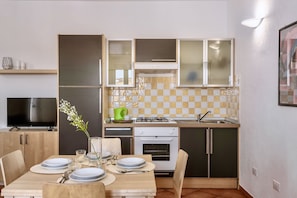 A compact kitchen with a dining area, featuring a stove, oven, and a television. - Residence con piscina a 300 mt dal mare (Santa Teresa di Gallura)